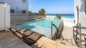 A pool area with lounge chairs, a view of the beach, and a white building with windows. - 4 BR Kikita Beach Villa Oceanfront w Pool (Dorado)