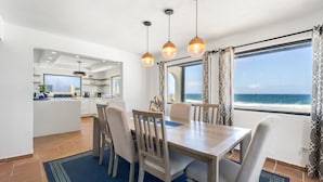 A dining area with a view of the ocean, a kitchen in the background, and a blue rug on the floor. - 4 BR Kikita Beach Villa Oceanfront w Pool (Dorado)