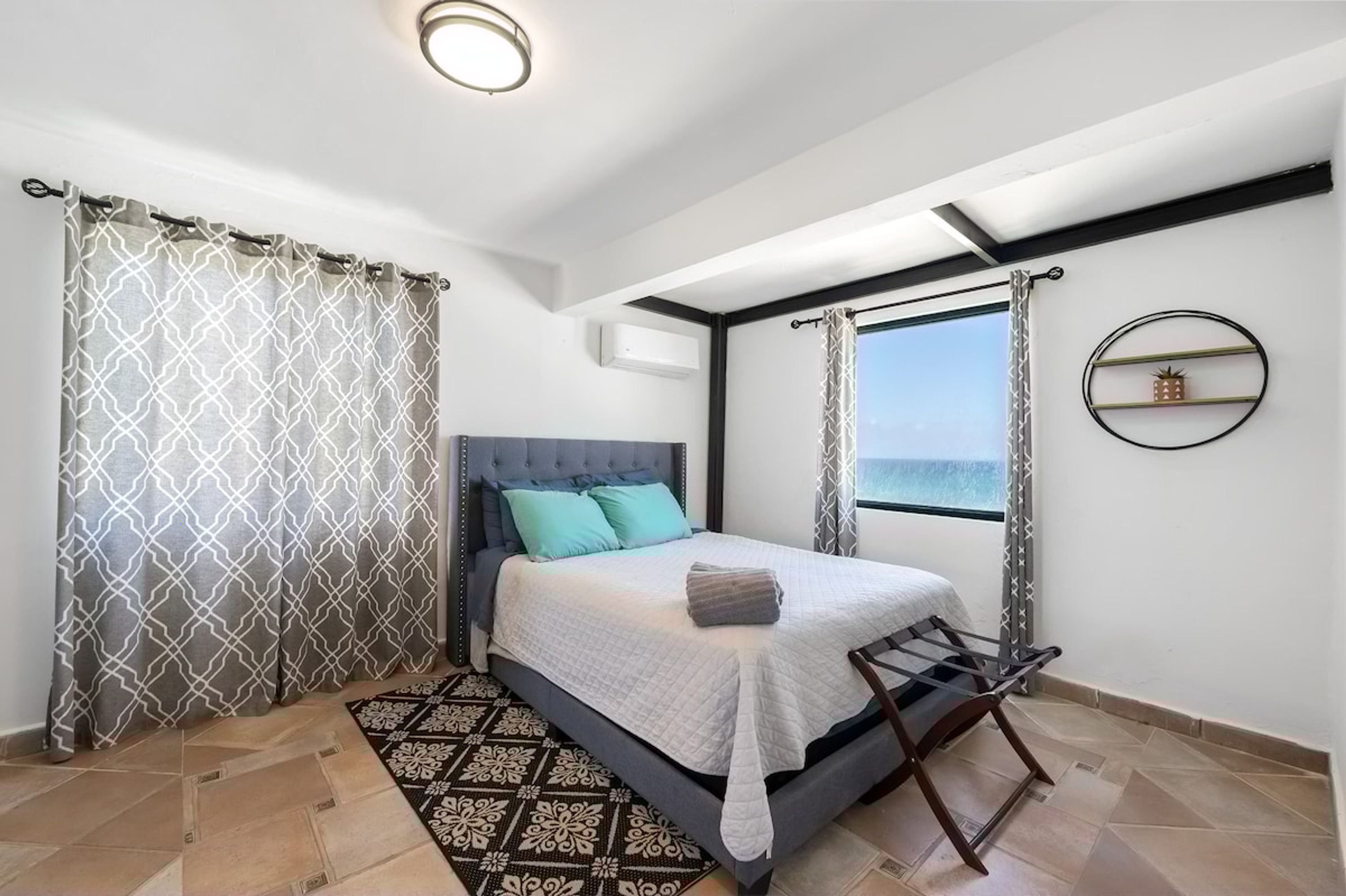 Una camera da letto con un letto, tende, una finestra, uno scaffale a parete e un tappeto decorato.