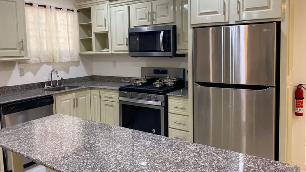 A kitchen with white cabinets, a stainless steel refrigerator, a microwave, a stove, and a granite countertop. - Gentlemen s Suite 3 Bedroom (Georgetown)