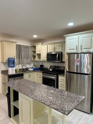 A kitchen with white cabinets, a granite countertop, a stainless steel refrigerator, a microwave, a stove, and a water dispenser. - Gentlemen s Suite 3 Bedroom (Georgetown)