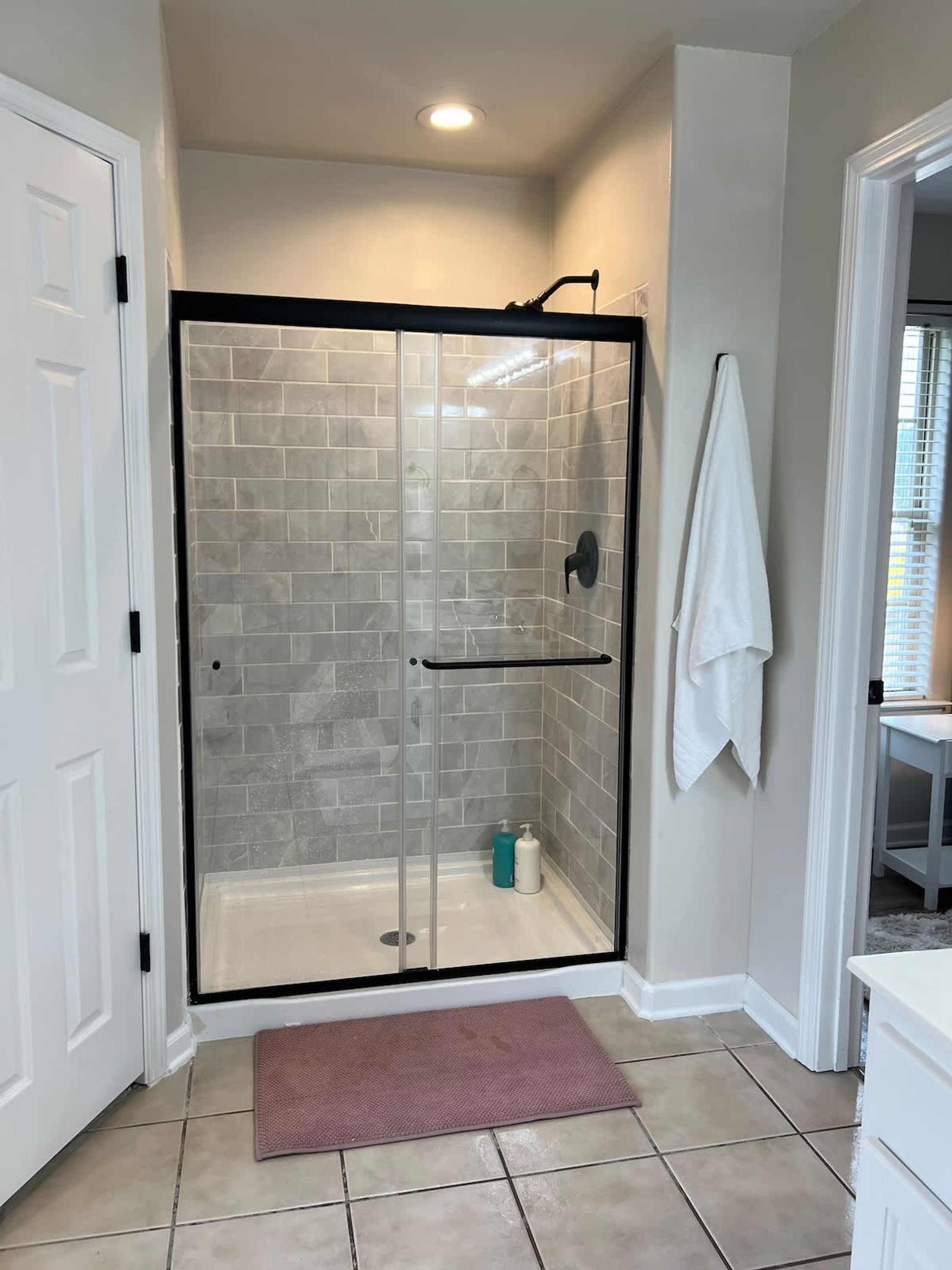 A walk-in shower with glass doors, a towel rack, and a small mat at the entrance.
