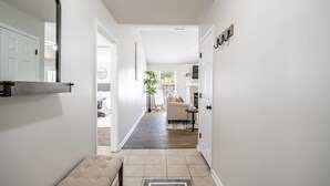 A hallway with a bench, a door, and a view into a living room with a sofa and a table. - Pool Oasis w King Bed Firepit (Cabot)