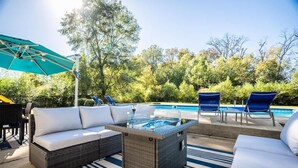 A poolside area with wicker furniture, a glass-top table, and lounge chairs. - Pool Oasis w King Bed Firepit (Cabot)