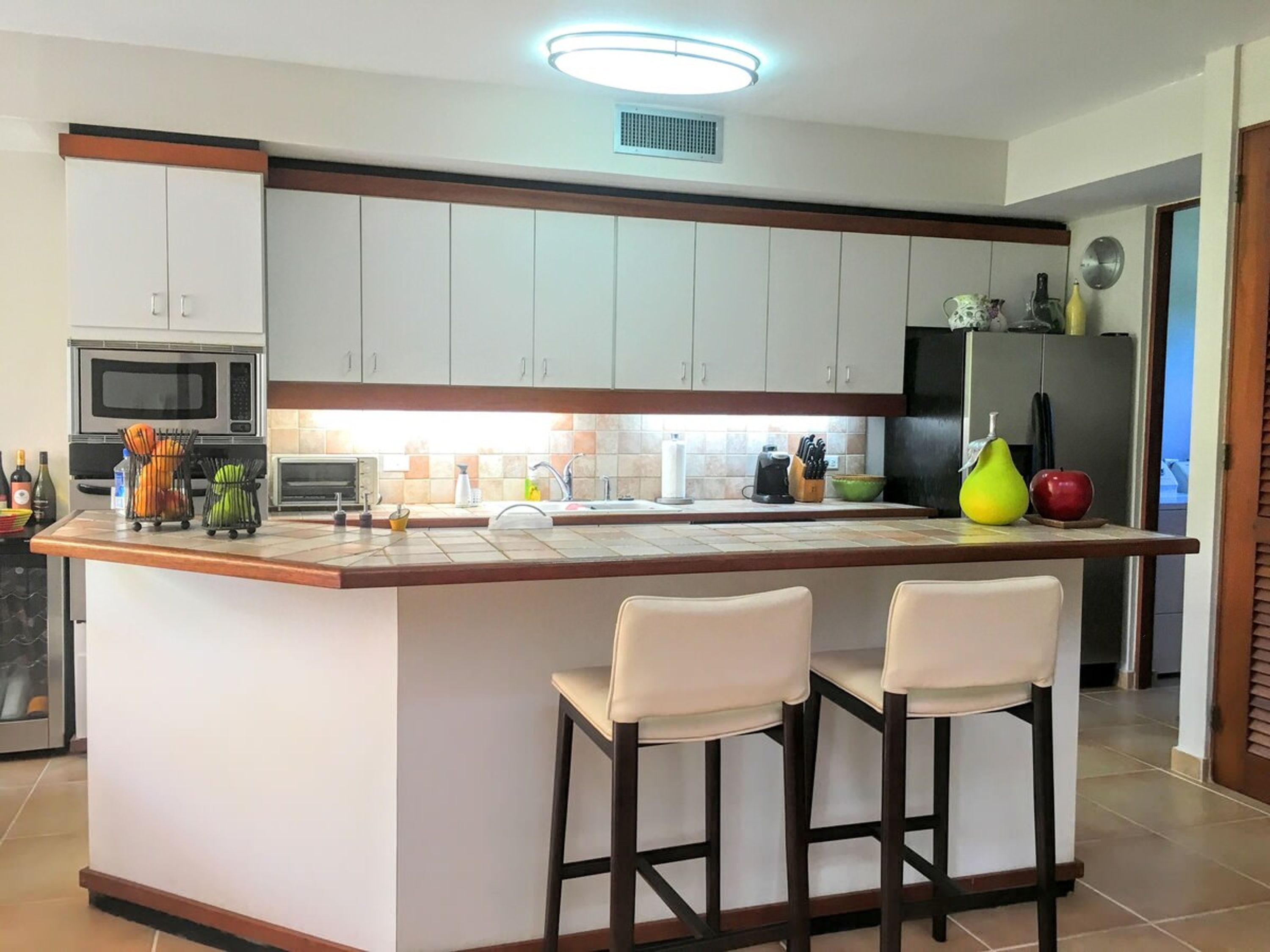 Una cocina moderna con armarios blancos, una isla central con dos taburetes de bar, un microondas, un tostador y diversos electrodomésticos.