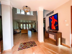 A spacious living area with a high ceiling, a large window, and a modern art piece on the wall.