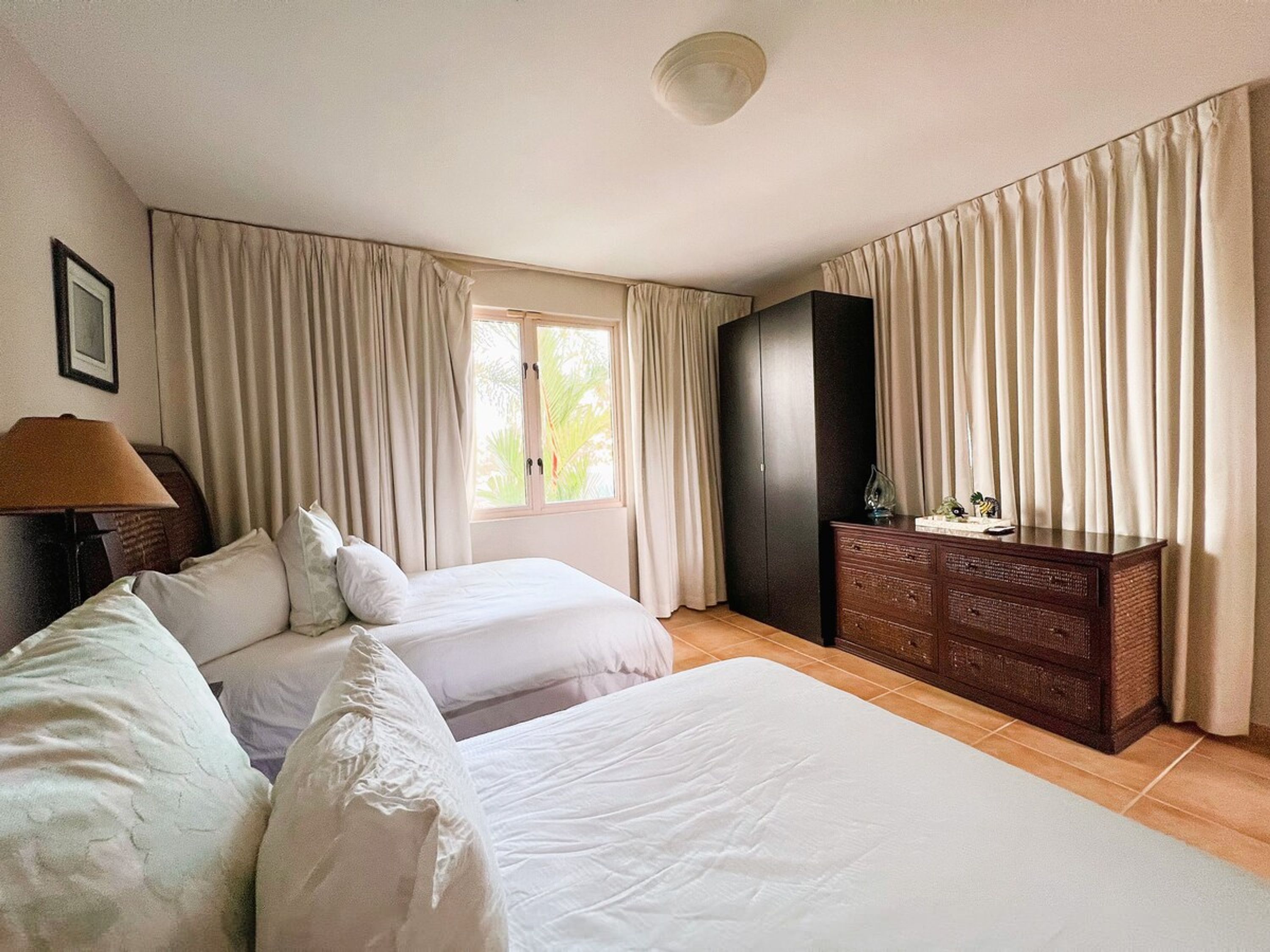 Ein Hotelzimmer mit zwei Betten, einem Schrank, einem Schreibtisch mit Lampe und einem Fenster mit Vorhängen.