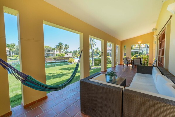 A spacious balcony with a hammock, wicker furniture, and a view of a well-maintained lawn and buildings. - Villa De Palma - Oceanfront Community w Generator (Vega Alta)