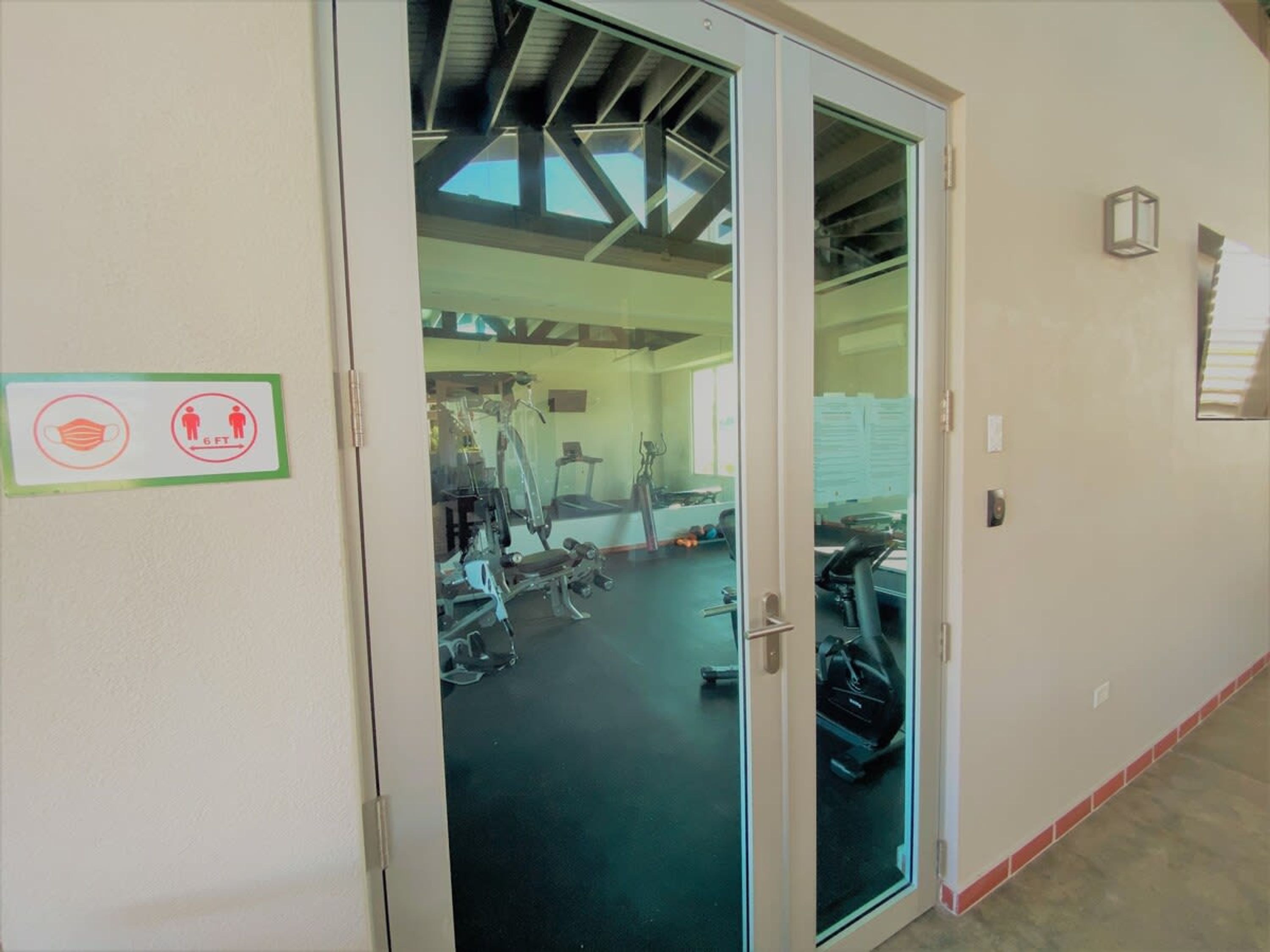 Une salle de sport équipée de matériel d’exercice, dotée d’une porte en verre et affichant un panneau indiquant les mesures de distanciation sociale.