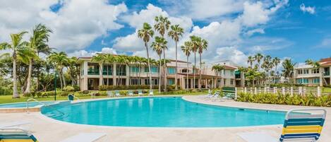 A pool area with lounge chairs, palm trees, and a building with multiple balconies.