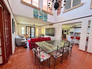 A spacious living area with a glass dining table, red sofas, and a kitchen in the background.