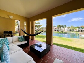 A spacious patio with a white sofa, a hammock, and a grill. A pool and buildings are visible in the background. - Villa De Palma - Oceanfront Community w Generator (Vega Alta)