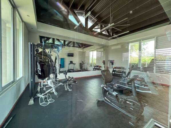 A modern gym with various exercise equipment, large windows, and a high ceiling. - Villa De Palma - Oceanfront Community w Generator (Vega Alta)