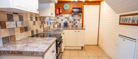 Una cocina compacta con encimera de granito, armarios blancos, horno empotrado, microondas y un refrigerador pequeño.