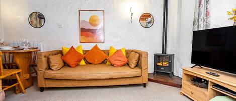 Una sala de estar acogedora con un sofá marrón, cojines de colores, un mueble de TV de madera, una chimenea y un comedor con mesa y sillas de madera.