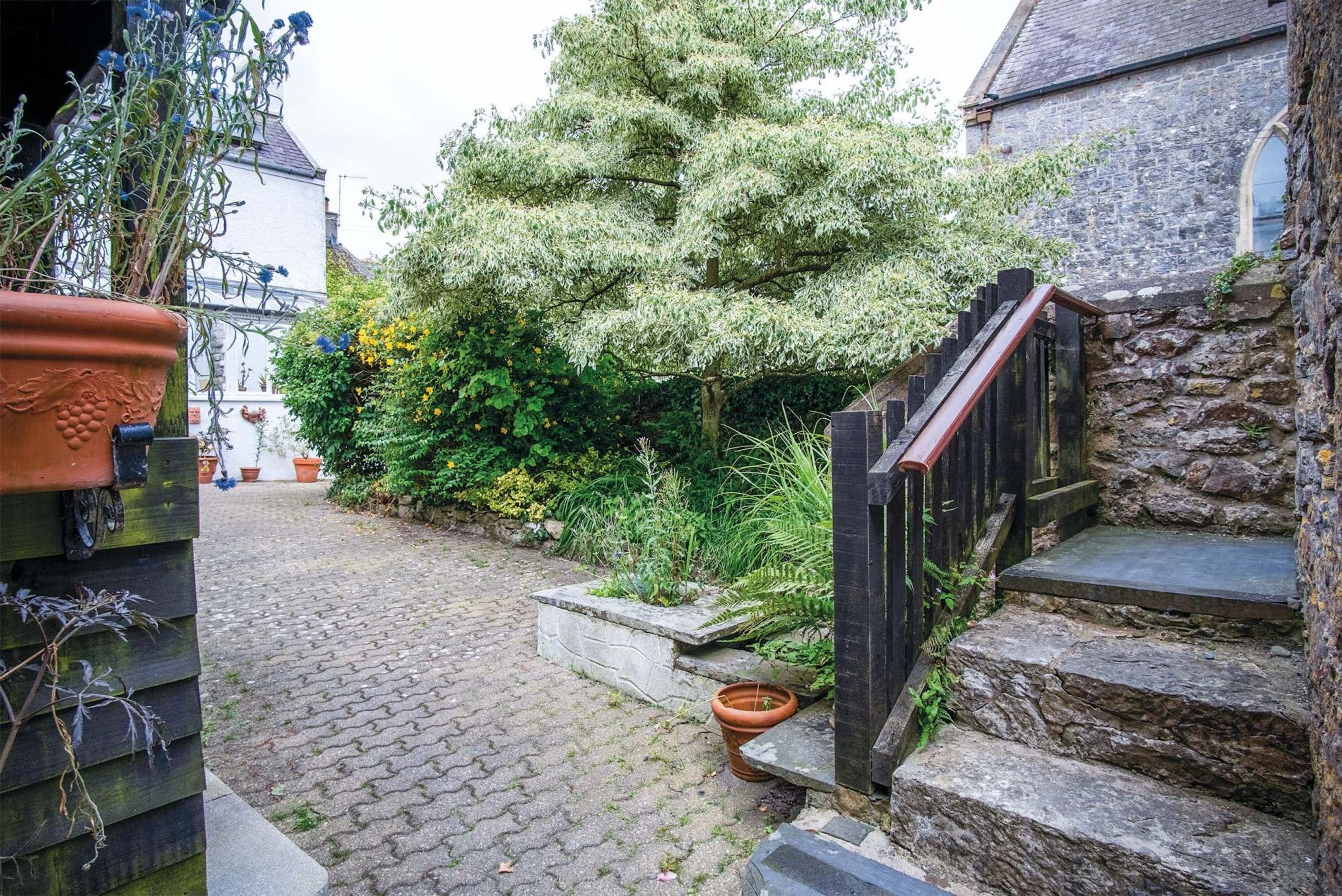 A cobblestone path leading to a stone staircase with a wooden handrail.