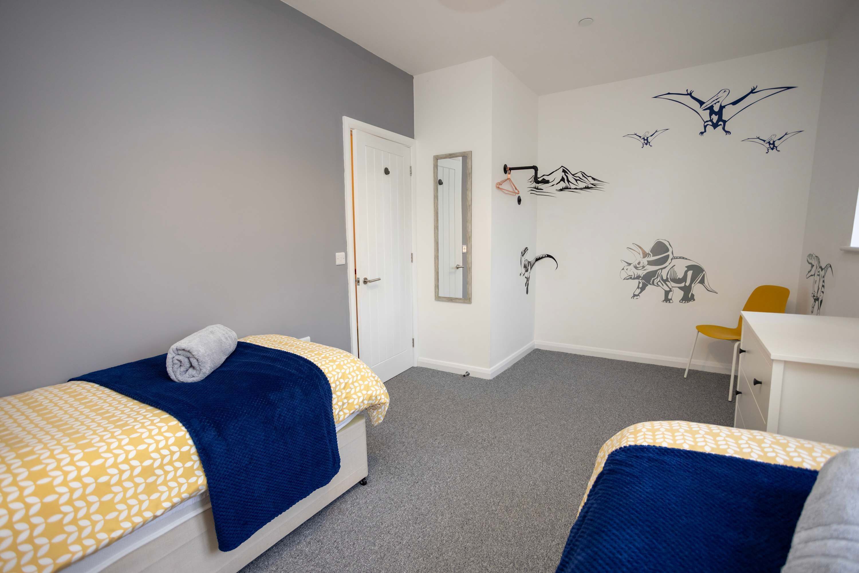 A bedroom with two beds, a desk, and a chair.