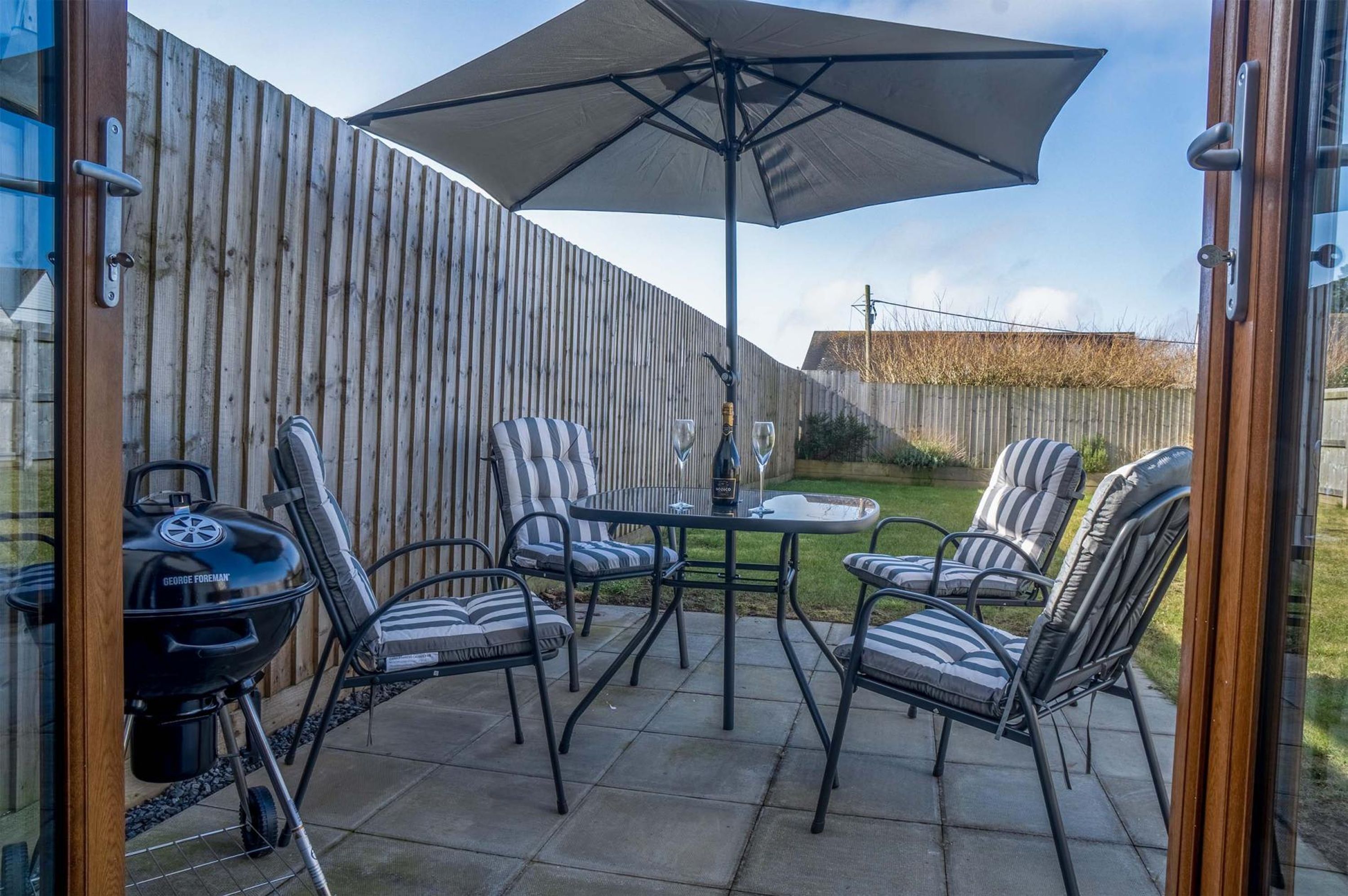 A patio with a grill, striped chairs, and a table under a large umbrella.