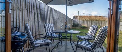 A patio with a grill, striped chairs, and a table under a large umbrella.