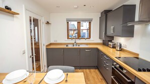 A compact kitchen with a wooden countertop, grey cabinets, a built-in oven, and a window with a view of the outside. - Johnnys Cove - 2 Bedroom House - New Hedges (Saundersfoot)