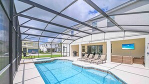 A covered outdoor swimming pool with lounge chairs and a television screen. - Super Size - 11br Spacious Home w Pool HOT TUB (Kissimmee)