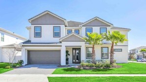 A two-story house with a garage, a front porch, and a well-maintained lawn with palm trees. - Super Size - 11br Spacious Home w Pool HOT TUB (Kissimmee)
