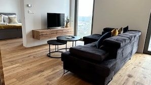 A modern living room with a dark sofa, a small round table, and a TV mounted on the wall.