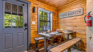 A rustic cabin interior with a gray door, wooden walls, a 'Farm Market' sign, a fire extinguisher, and a table set with plates and glasses.