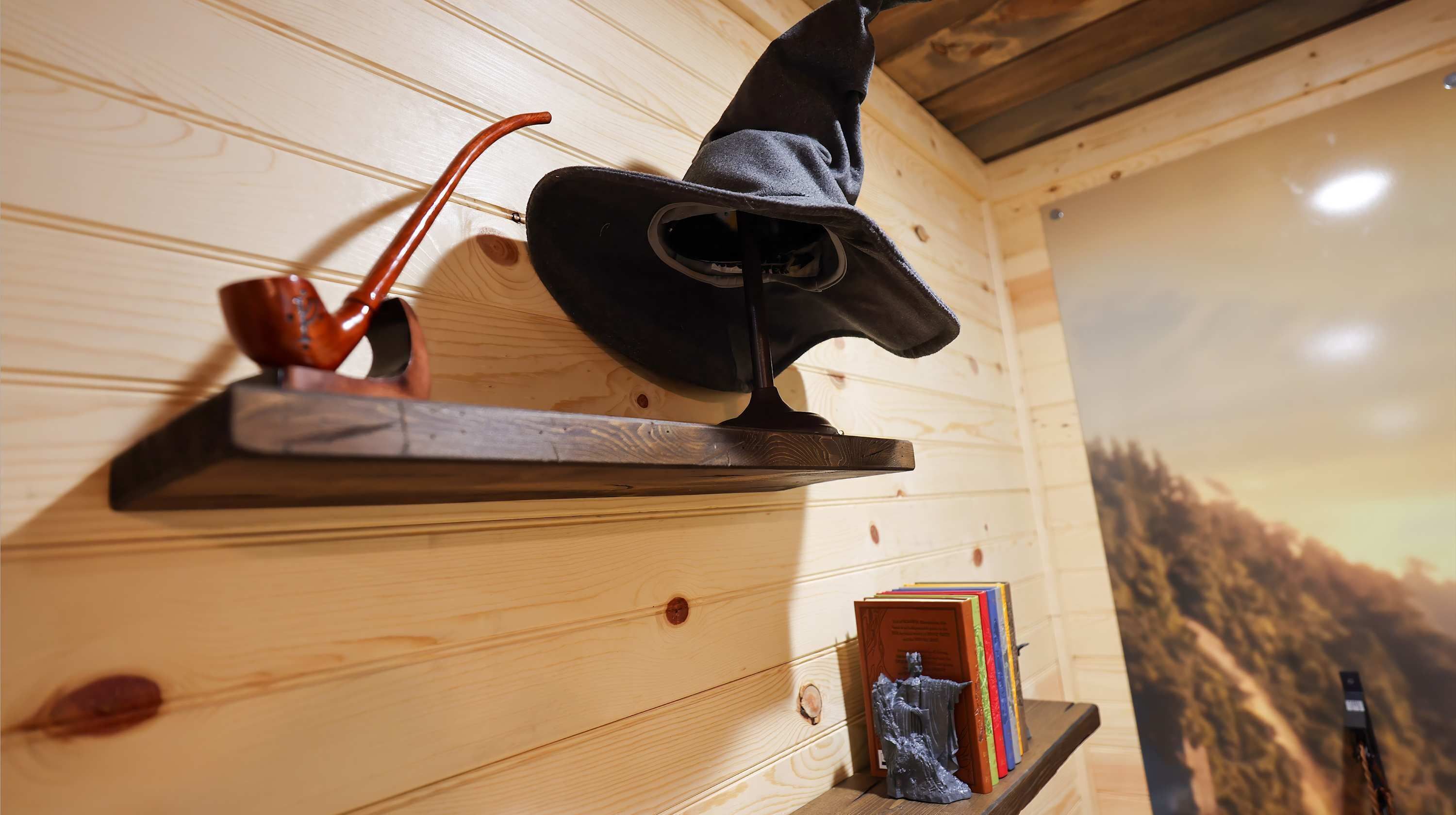 Een houten interieur met een plank waarop een hoed, pijp en boeken staan.