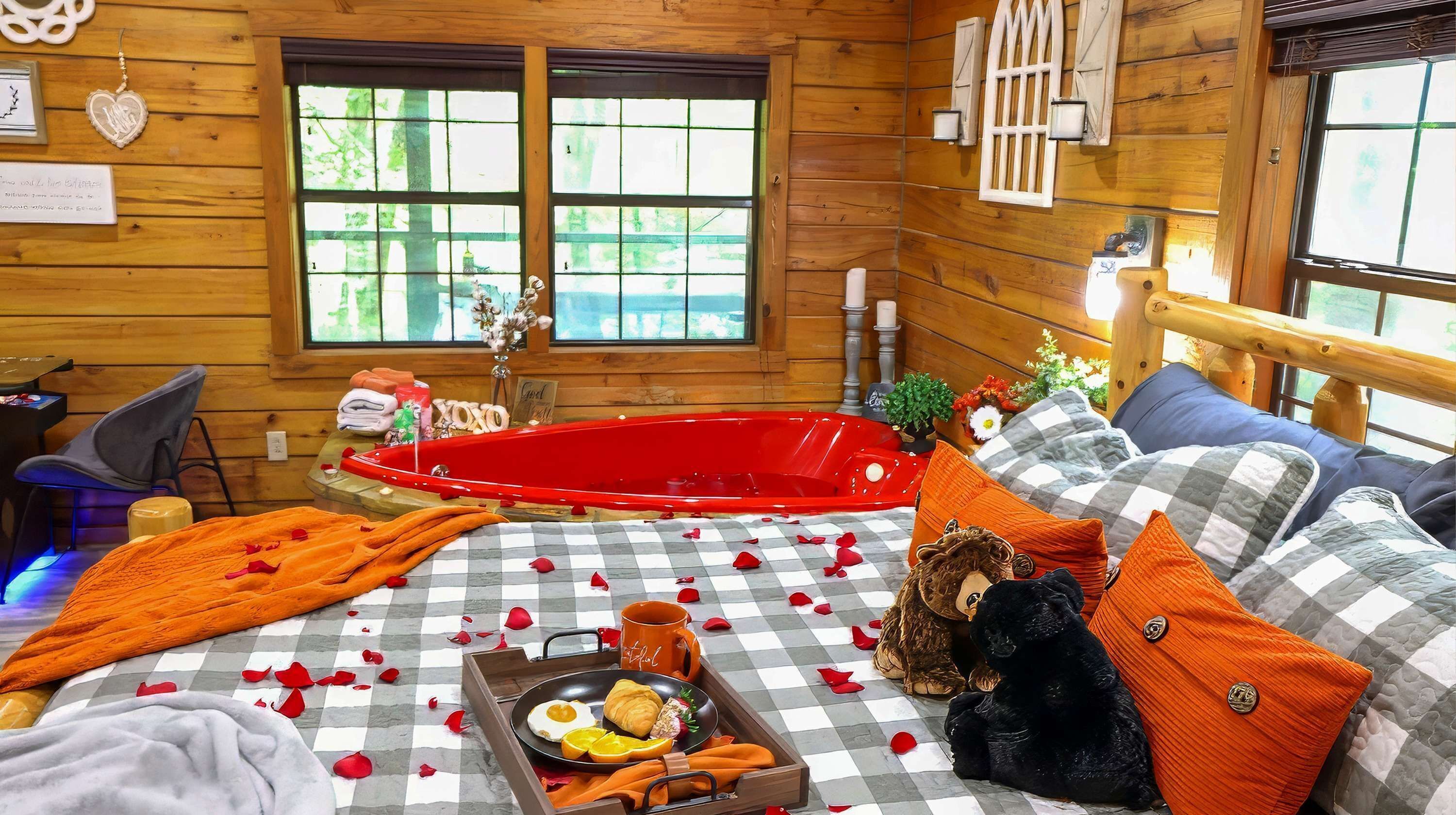 Ein gemütliches Cabin-Zimmer mit kariertem Boden, einer roten Badewanne, einem Bett mit blau-orangenen Kissen und einem Frühstücksbrett mit Eiern und Gebäck.