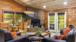 L’intérieur chaleureux d’un chalet avec une cheminée en pierre, des murs en bois et un téléviseur fixé au-dessus.