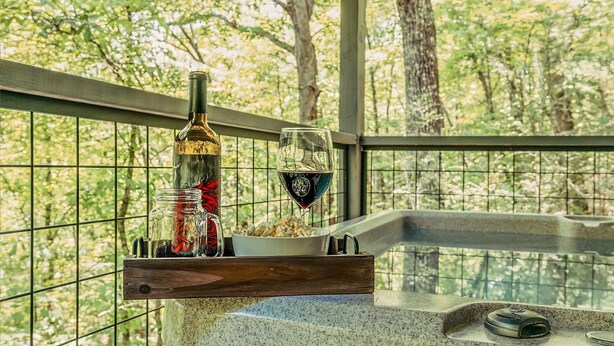 Un verre de vin rouge sur un balcon, accompagné d’une bouteille de vin, d’un verre d’eau et d’un bol de pop-corn.