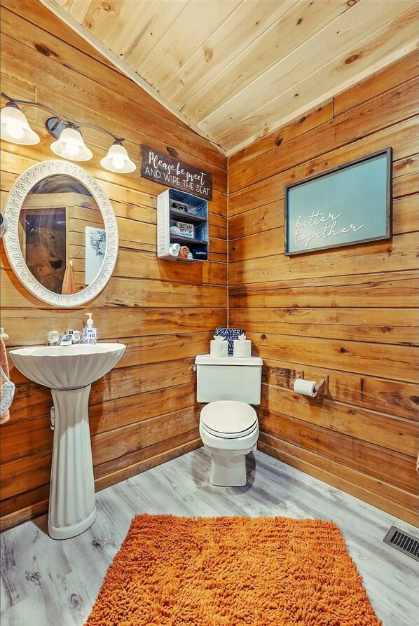 Un baño de cabaña de madera con lavamanos pedestal, inodoro y espejo.
