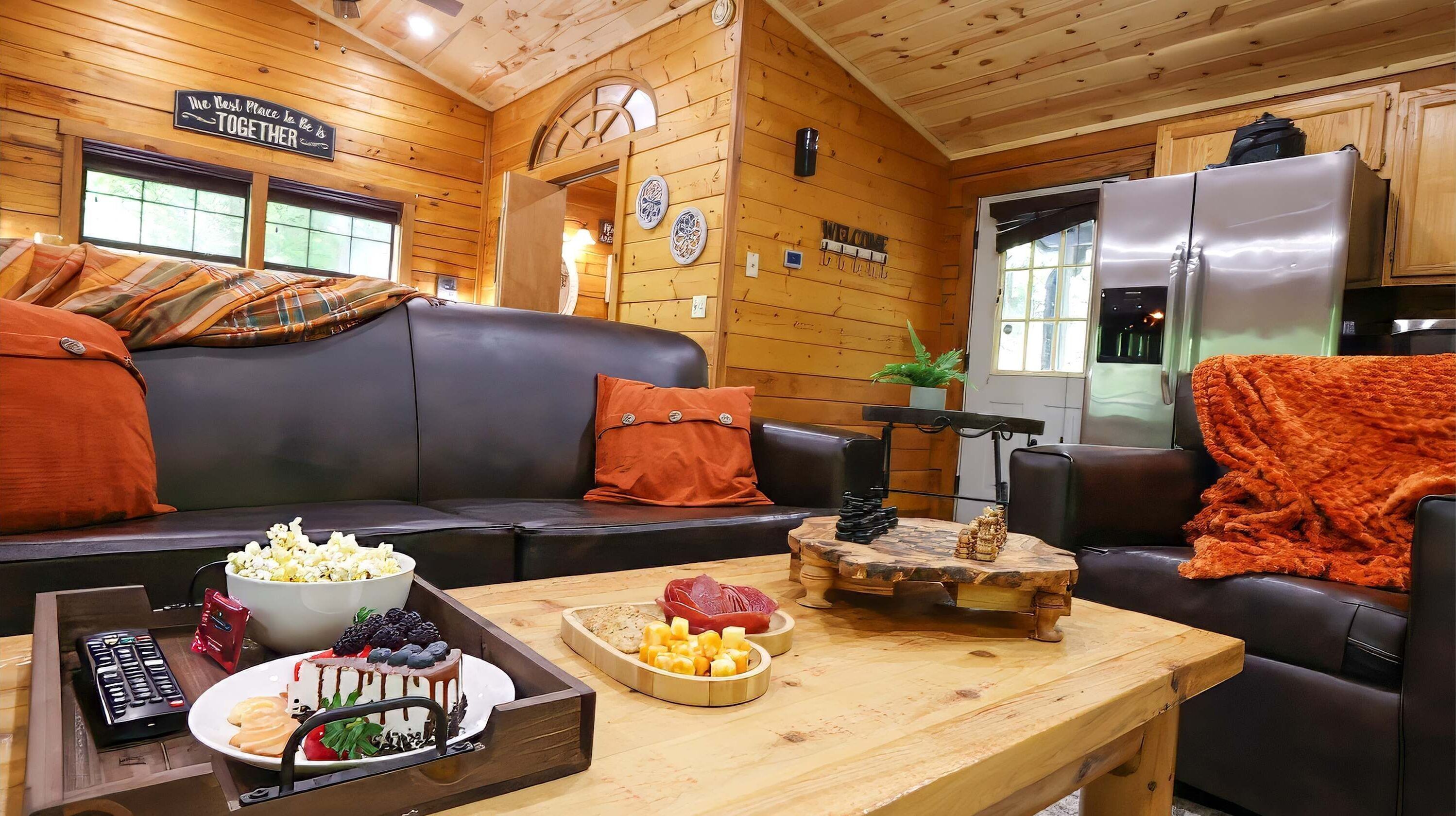 A cozy cabin interior with a wooden interior, a sofa, a dining table with snacks, and a refrigerator.