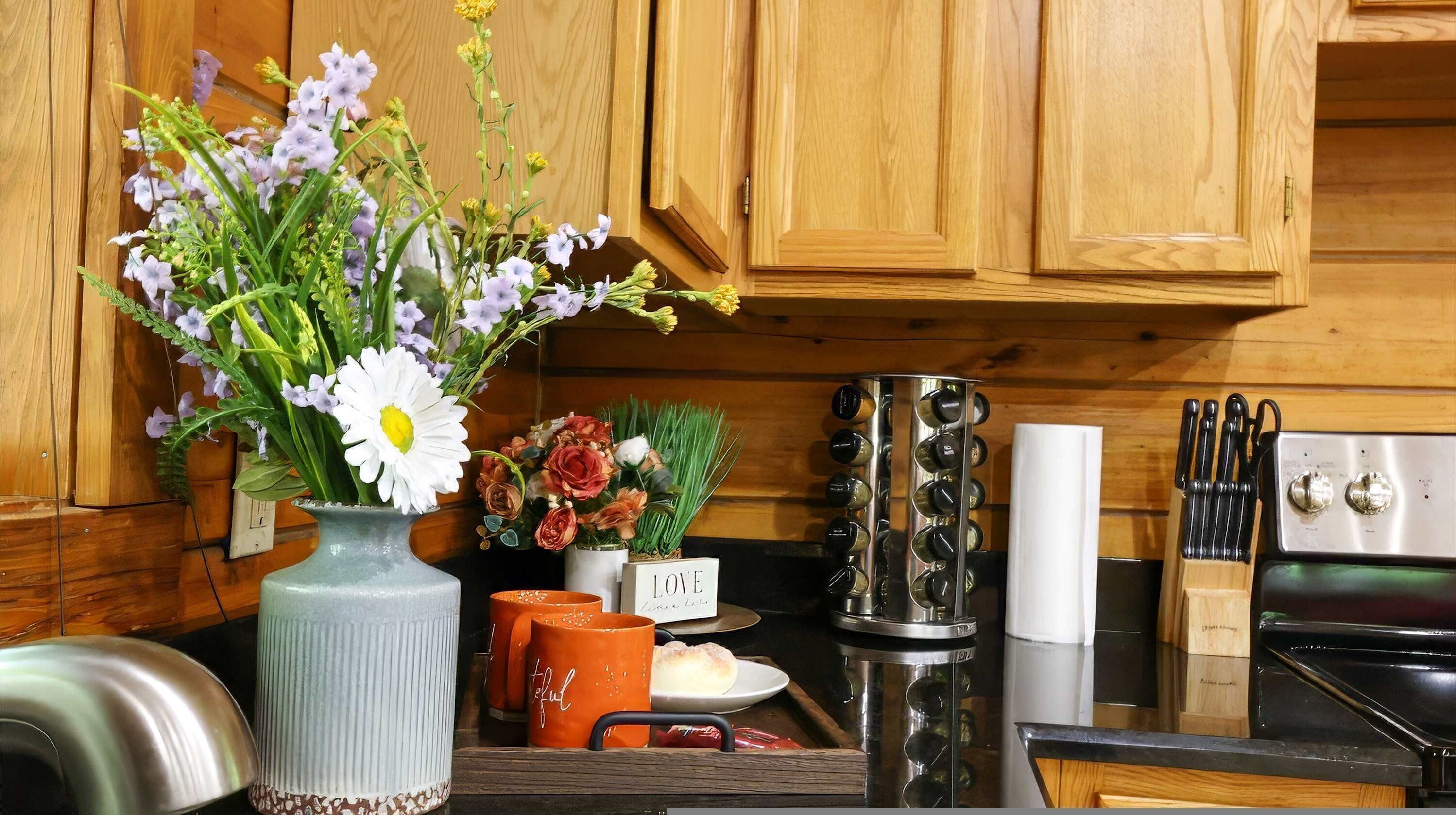 A kitchen with wooden cabinets, a stainless steel range, a coffee maker, and a vase with flowers.
