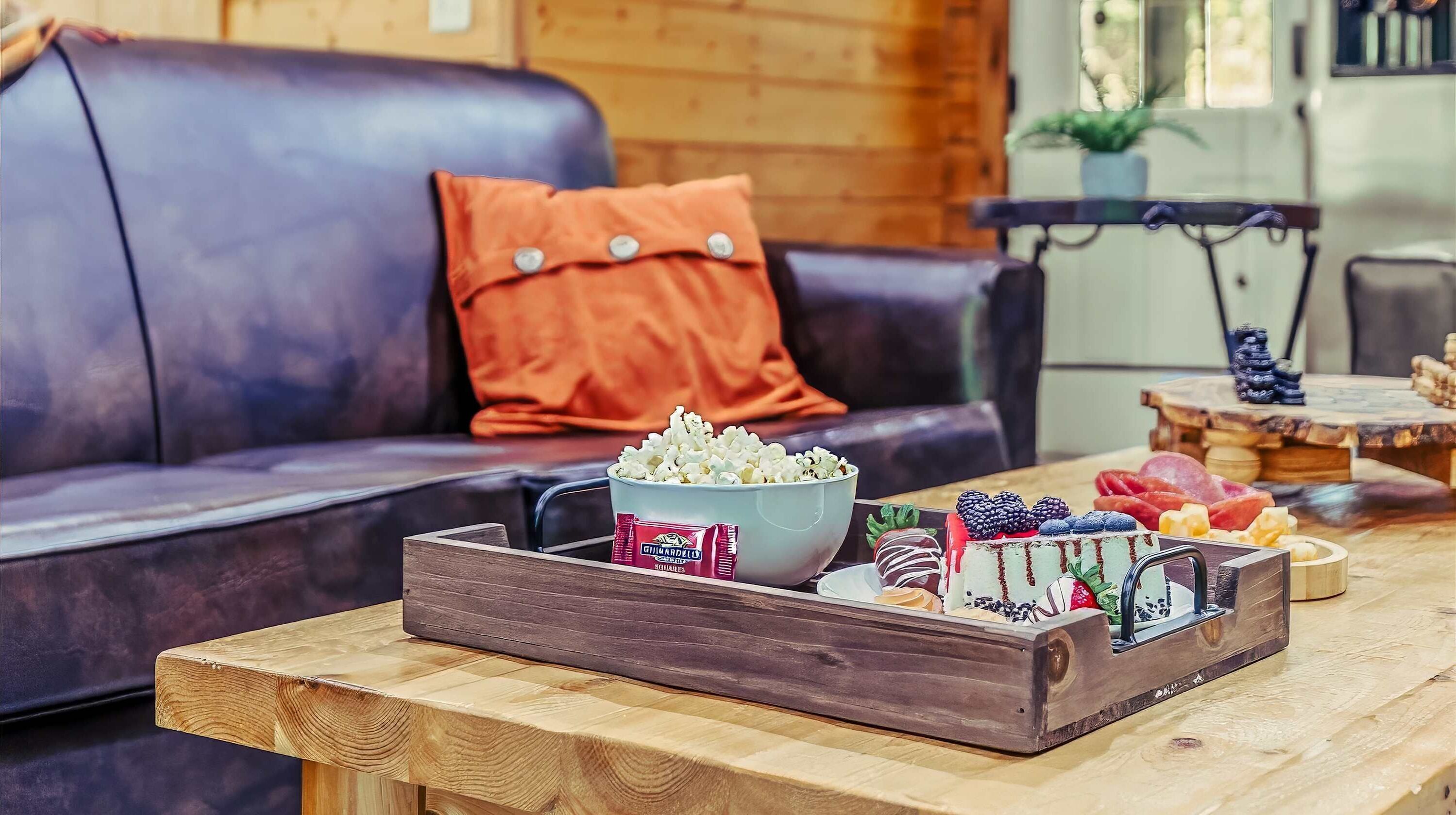 A wooden table with a tray holding popcorn, a bowl of snacks, and a cake with berries.
