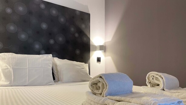 A hotel room with a neatly made bed, white pillows, a headboard with a circular pattern, and a wall-mounted light. - Fisherman s Albufeira Cosy Studio (Albufeira)