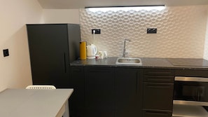 A compact kitchen with a modern design, featuring a black refrigerator, a sink with a faucet, and a built-in oven. - Fisherman s Albufeira Cosy Studio (Albufeira)
