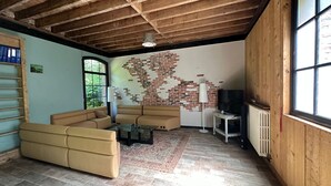 A living room with a brick wall, a sofa, a TV, and a window. - Ancienne Orangerie Du Chateau (Les Hauts-de-Caux)