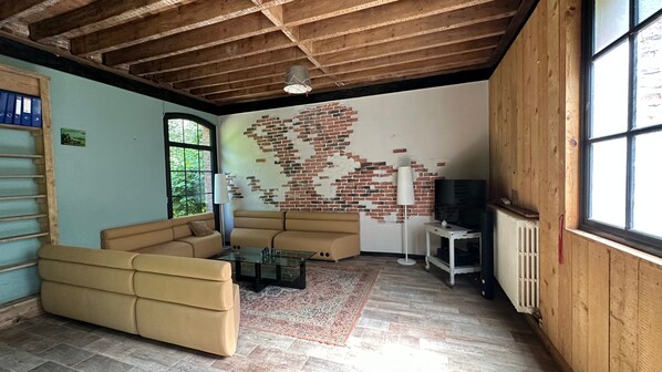 Una sala de estar con pared de ladrillo, un sofá, un televisor y una ventana.