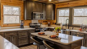 A modern kitchen with dark wooden cabinets, stainless steel appliances, and a central island with seating. - Bigfoot Bunkhouse Pool Views Theater Arcade Firepit Book Now (Sevierville)
