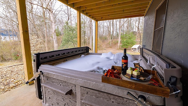 A hot tub with a wooden deck, a wine bottle, and a small figurine on the edge. - Bigfoot Bunkhouse Pool Views Theater Arcade Firepit Book Now (Sevierville)