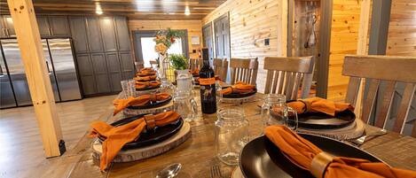 A wooden interior with a dining table set for four, featuring black plates, orange napkins, and clear glassware.