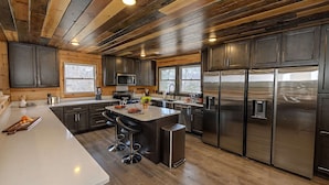 A modern kitchen with dark cabinets, stainless steel appliances, and a wooden ceiling. - Bigfoot Bunkhouse Pool Views Theater Arcade Firepit Book Now (Sevierville)