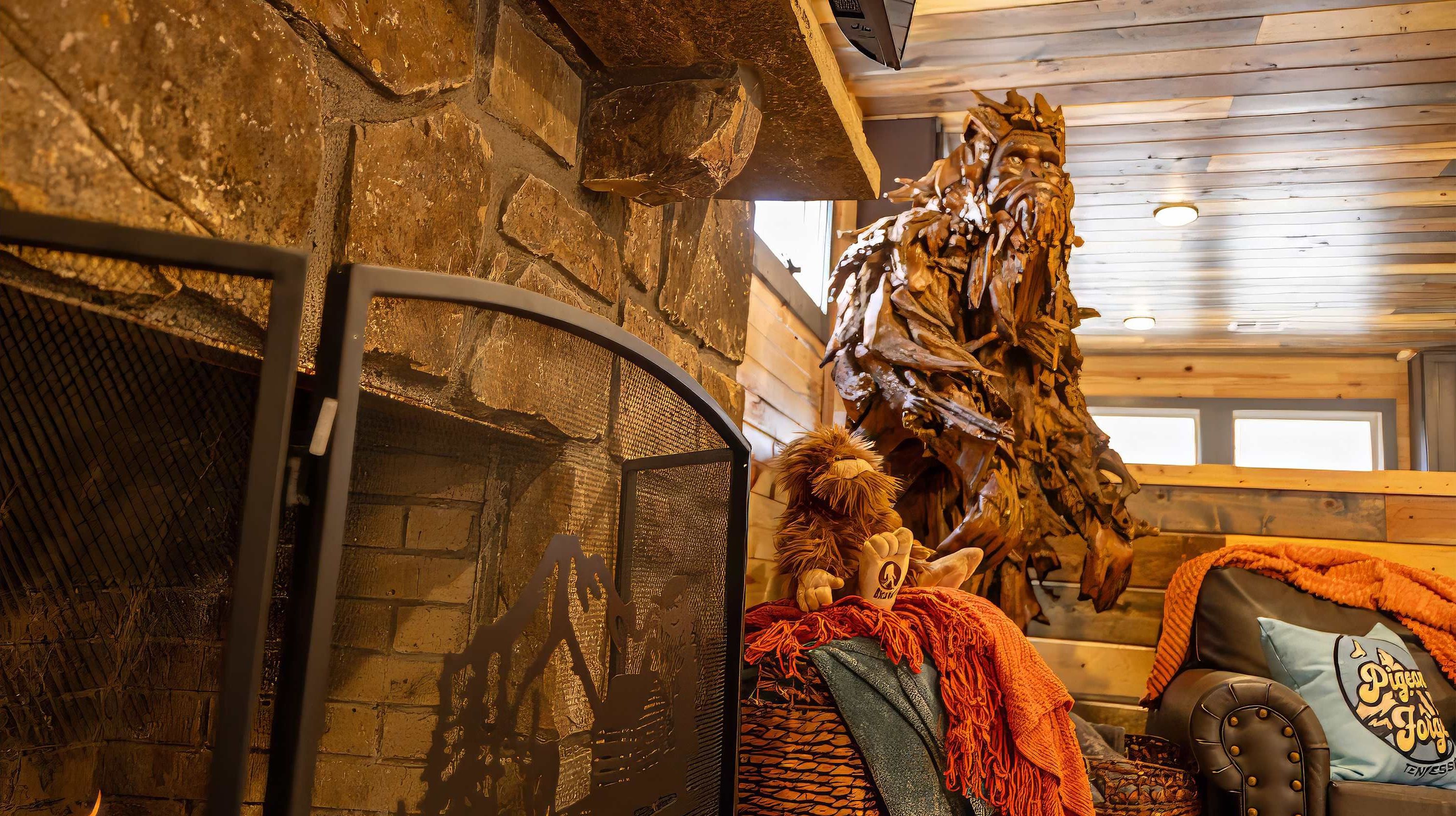 Un intérieur chaleureux avec une cheminée en pierre, une grande sculpture en bois et un fauteuil moelleux.