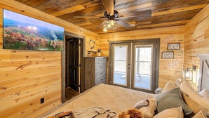 A cozy wooden room with a bed, a television, and a ceiling fan. - Bigfoot Bunkhouse Pool Views Theater Arcade Firepit Book Now (Sevierville)