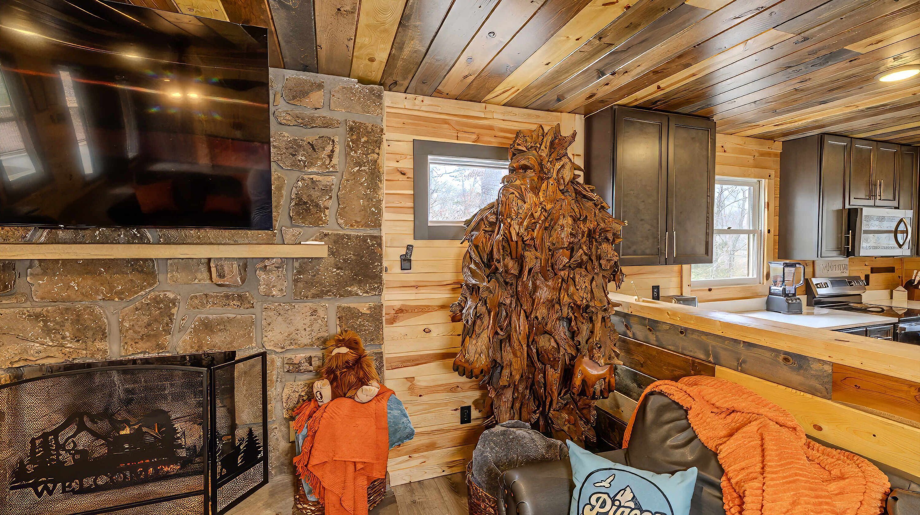 A rustic cabin interior with a stone fireplace, wooden walls, and a large wooden sculpture.
