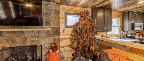 A rustic cabin interior with a stone fireplace, wooden walls, and a large wooden sculpture.