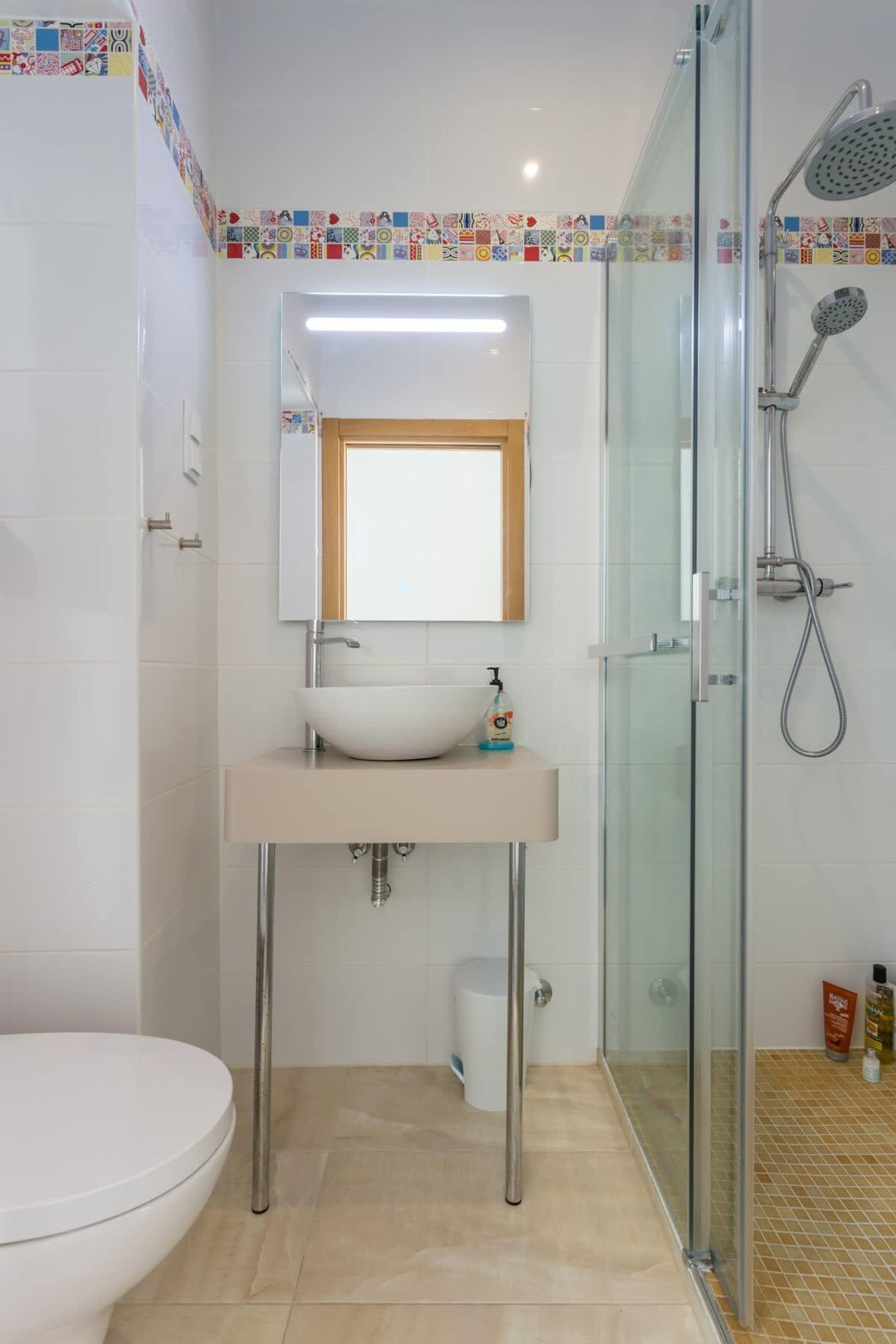 A bathroom with a glass-enclosed shower, a white sink with a mirror above, and a toilet.