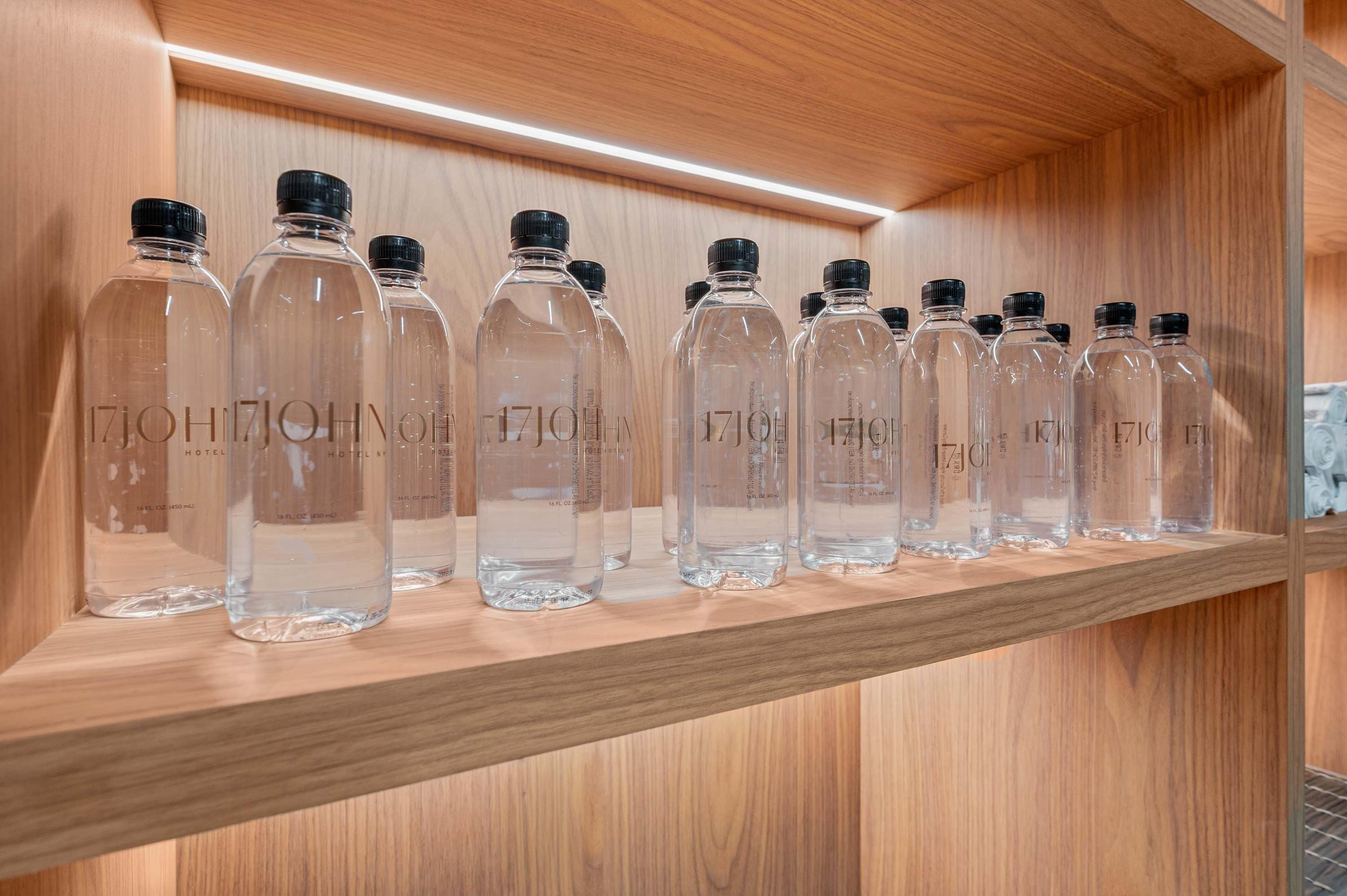 A wooden shelf with clear glass bottles labeled '17JOHN HOTEL' in a hotel setting.